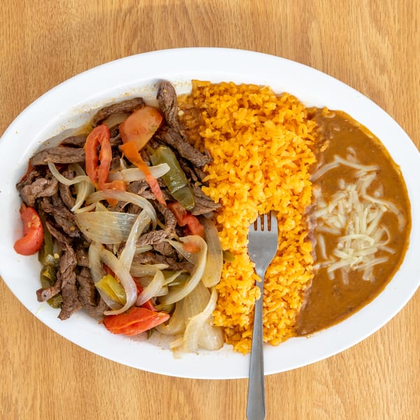 Plate of grilled steak strips with onions, tomatoes, and peppers, served with orange rice, beans, and a fork.