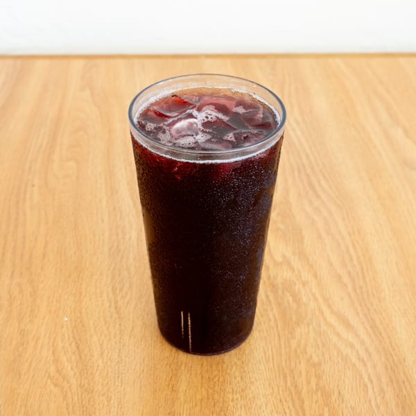 Tall glass of dark iced soda on a wooden restaurant table.