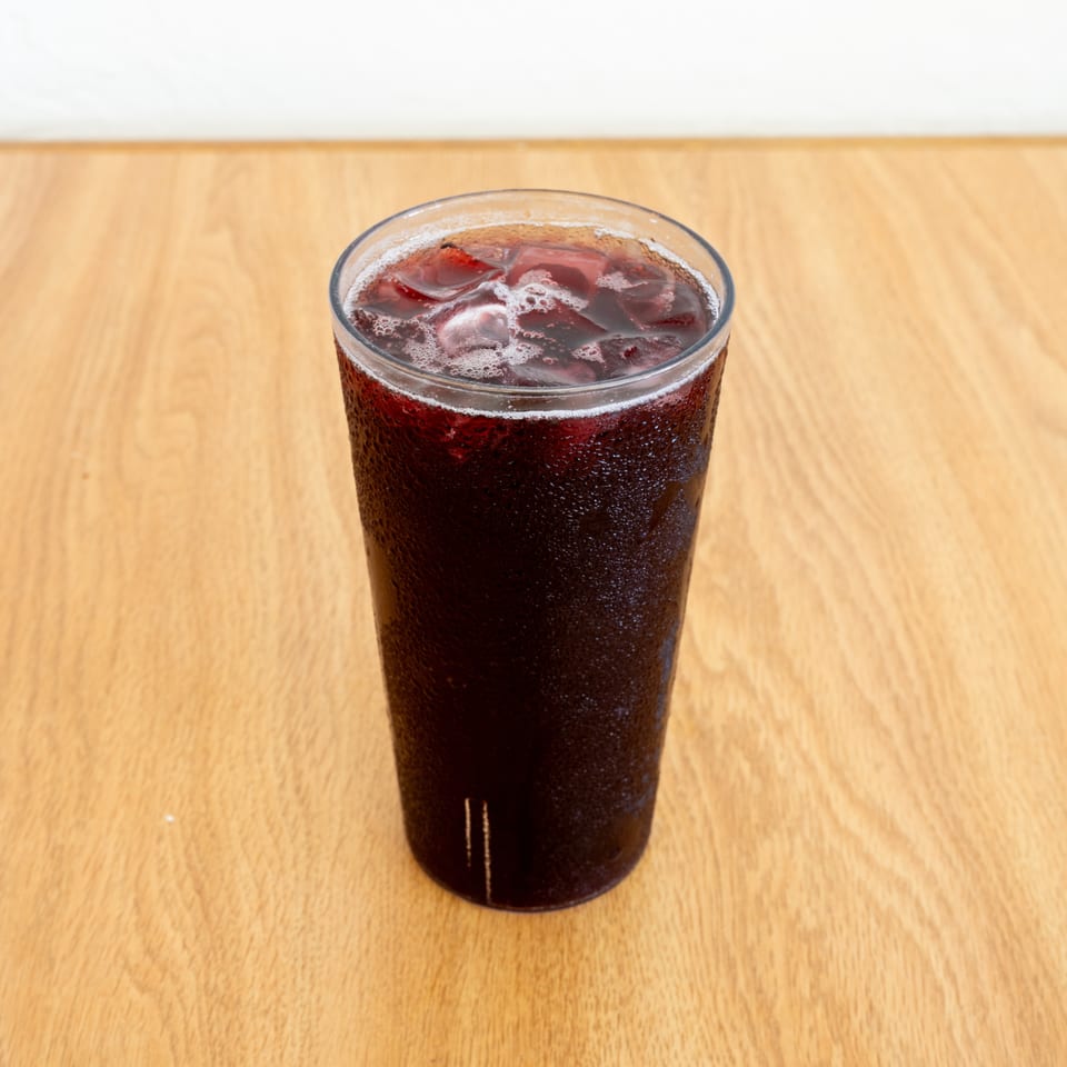 Tall glass of dark iced soda on a wooden restaurant table.