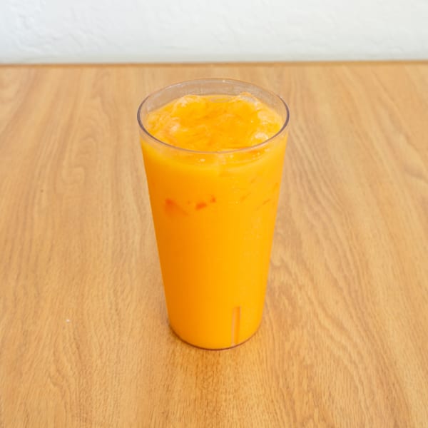 A clear cup holds a bright orange frozen drink on a wooden restaurant table.