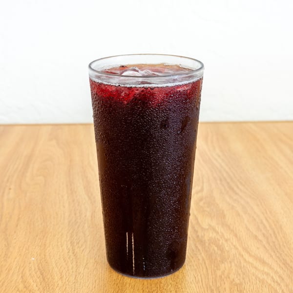 Tall glass of dark cola with ice and condensation sits on a wooden restaurant table.