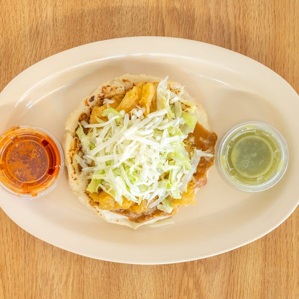 Plate of a folded Mexican-style dish topped with shredded lettuce, alongside red salsa and green sauce.