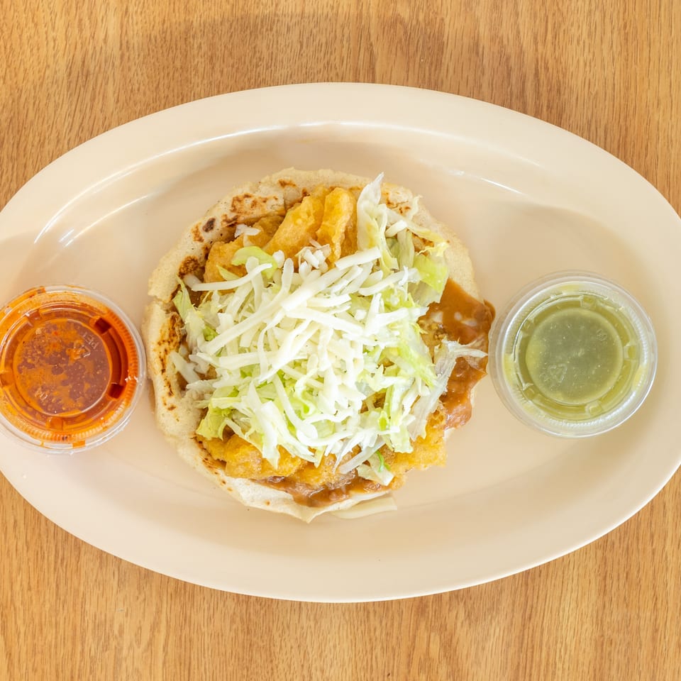 Plate of a folded Mexican-style dish topped with shredded lettuce, alongside red salsa and green sauce.