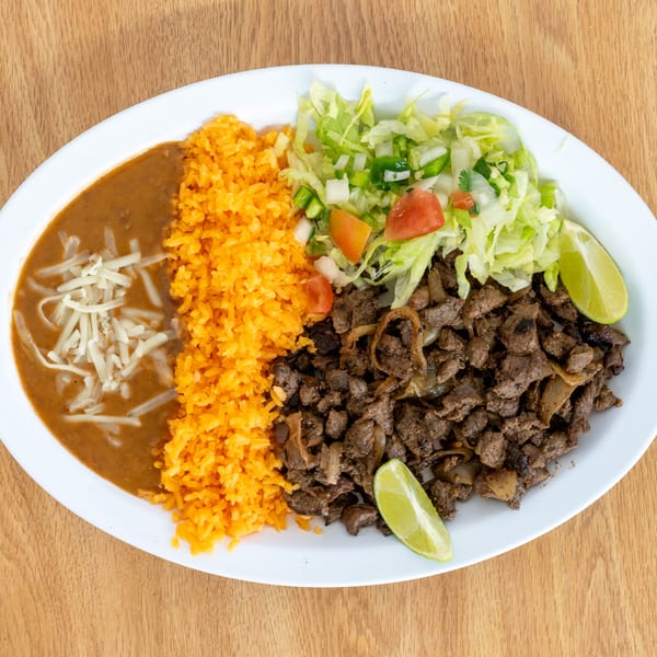 Plate of grilled beef with onions, Mexican rice, refried beans topped with cheese, lettuce salad, and lime wedges.