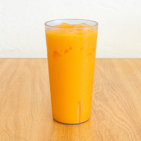 Tall glass of bright orange iced beverage on a wooden restaurant table.