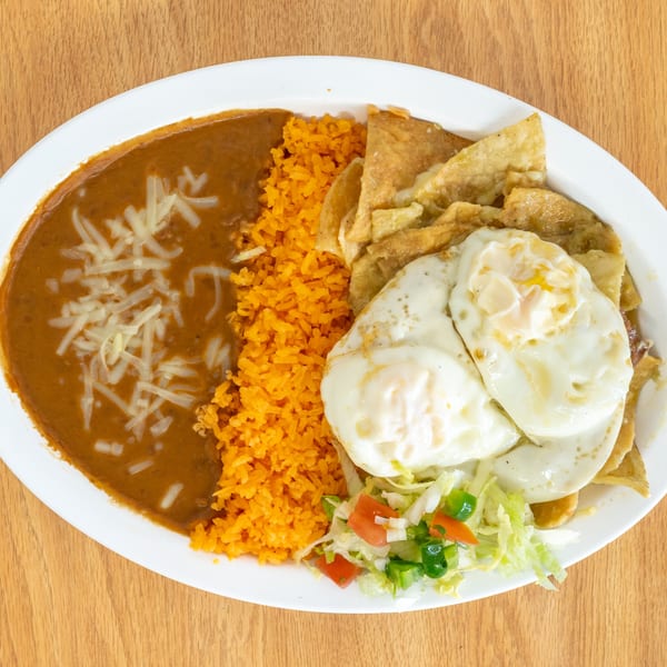 Mexican platter with orange rice, refried beans topped with cheese, crispy tortillas, fried eggs, and fresh salad.